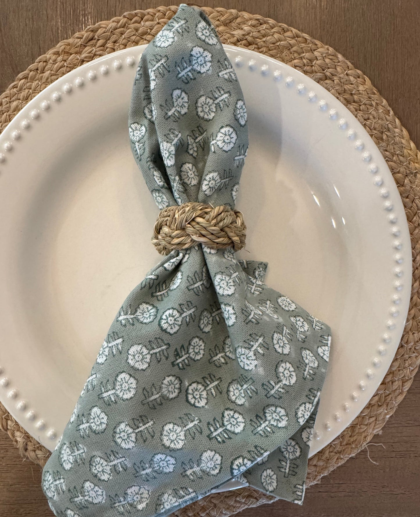 Green floral-patterned napkin in a woven napkin ring on a white plate and jute placemat