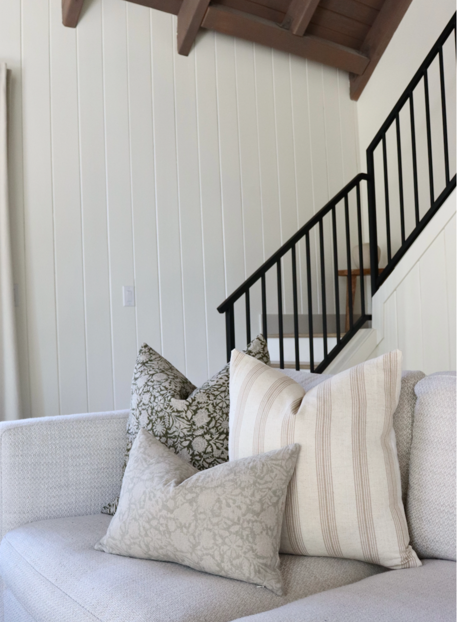 Gray sofa with patterned pillows in a room with a staircase and white walls.