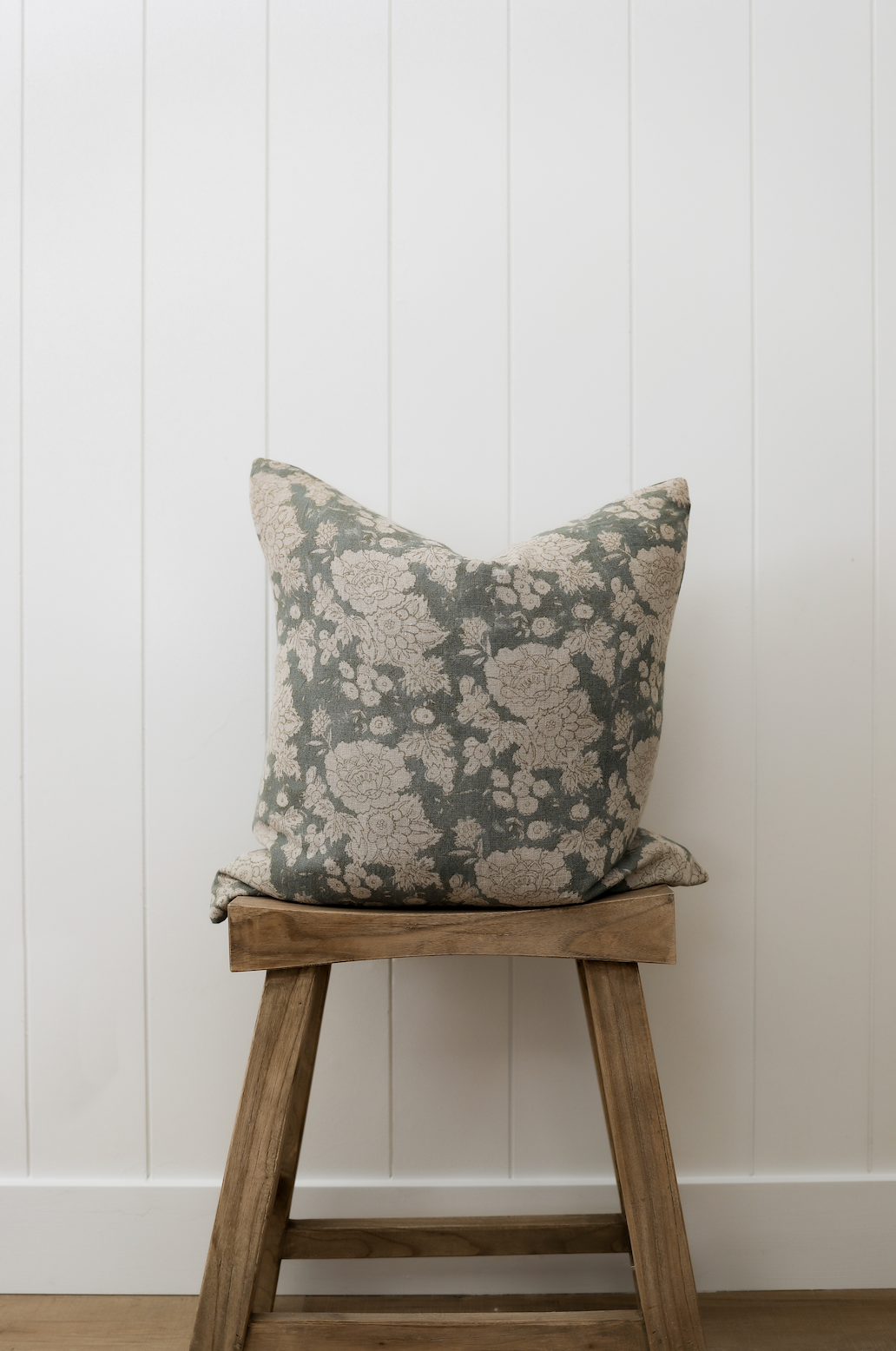 Decorative pillow on a wooden stool against a white paneled wall