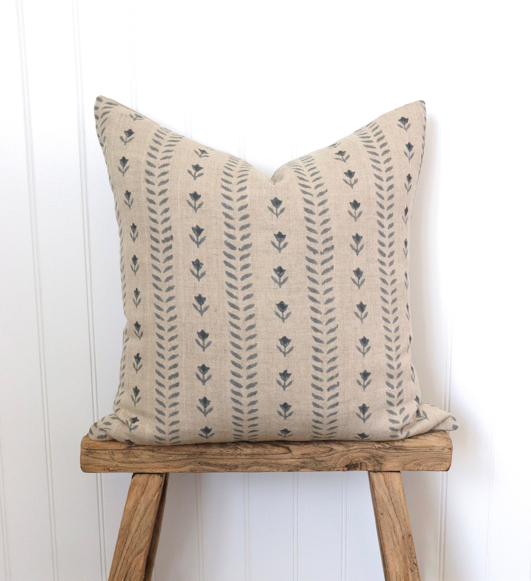 Decorative pillow with floral pattern on a wooden stool against a white wall