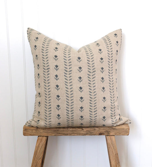 Decorative pillow with floral pattern on a wooden stool against a white wall