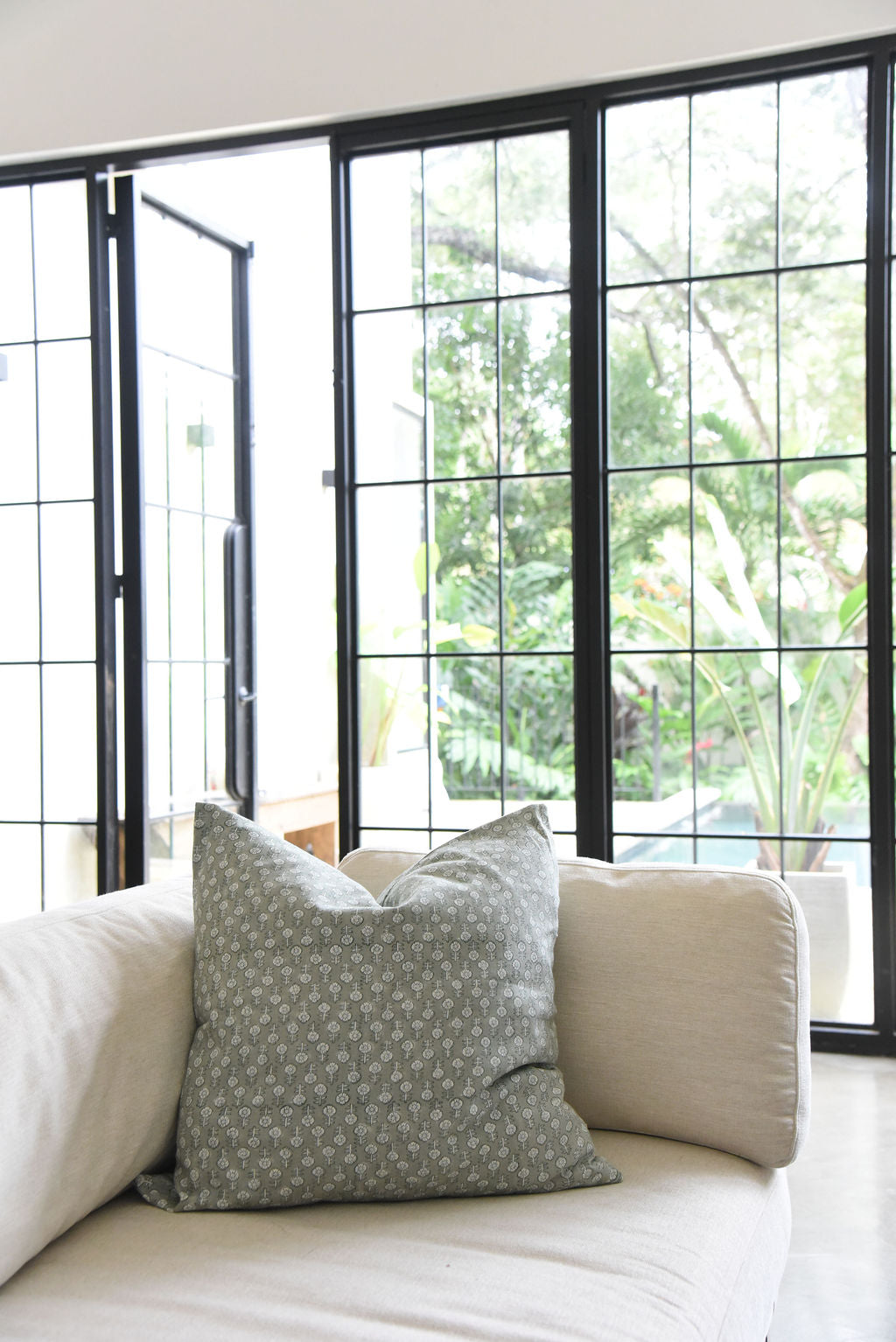 cream sofa with green block print floral patterned throw pillowin a room with large black windows.