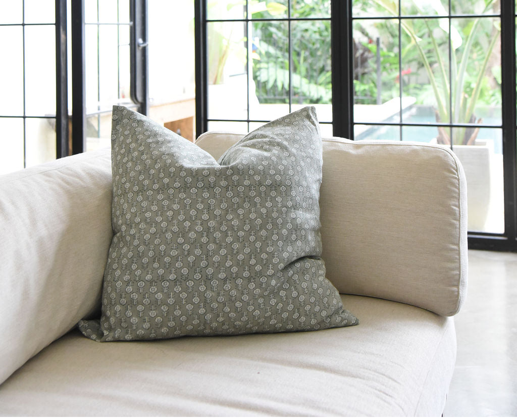 Greenish Gray patterned pillow on a beige sofa with a window in the background