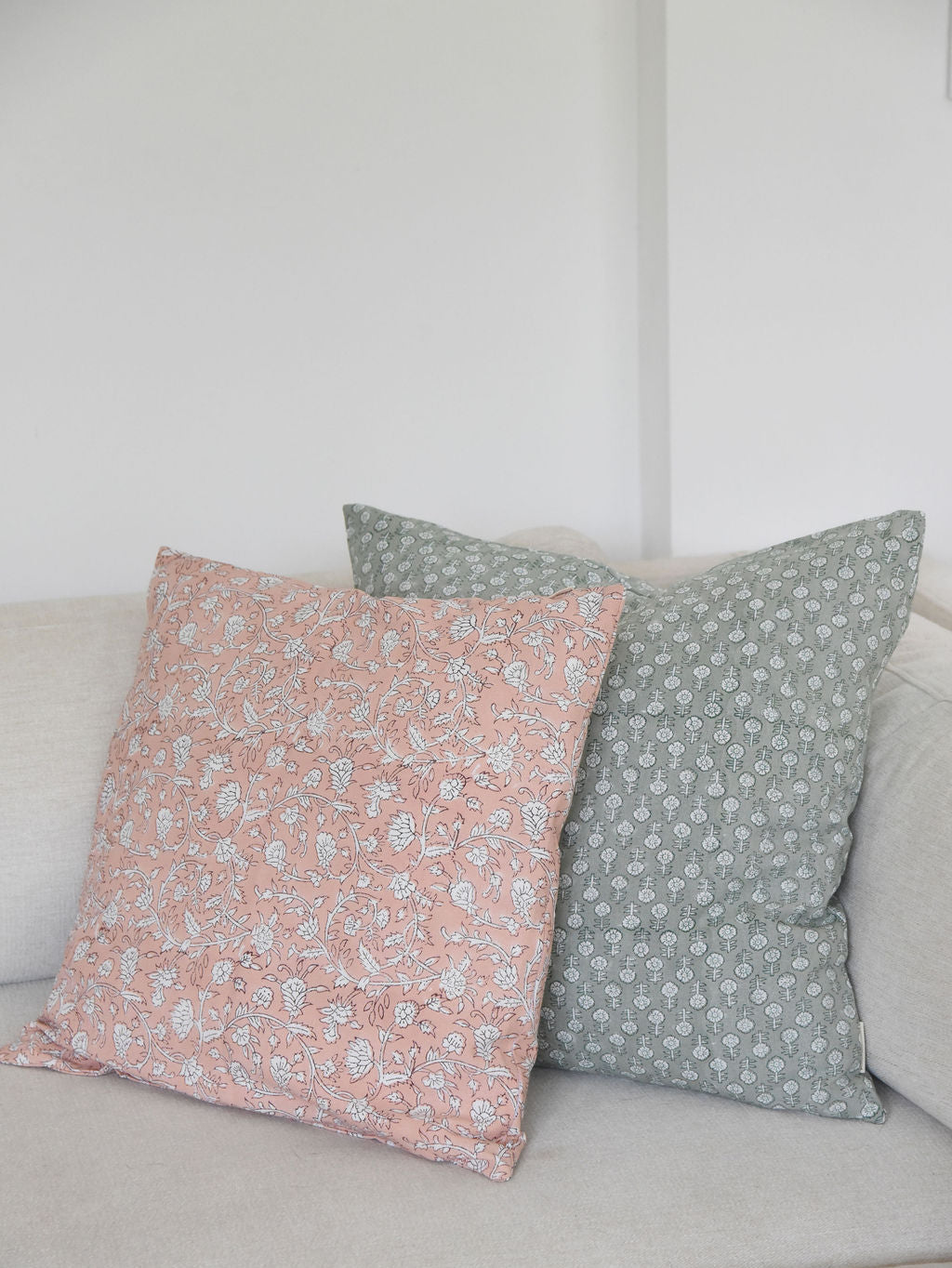 pink and green block print floral-patterned throw pillow cushions on a light-colored sofa against a white wall.