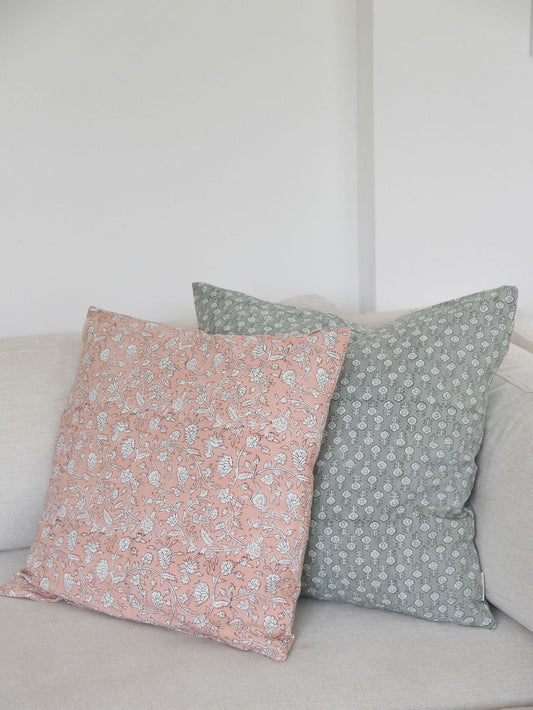pink and green block print floral-patterned throw pillow cushions on a light-colored sofa against a white wall.