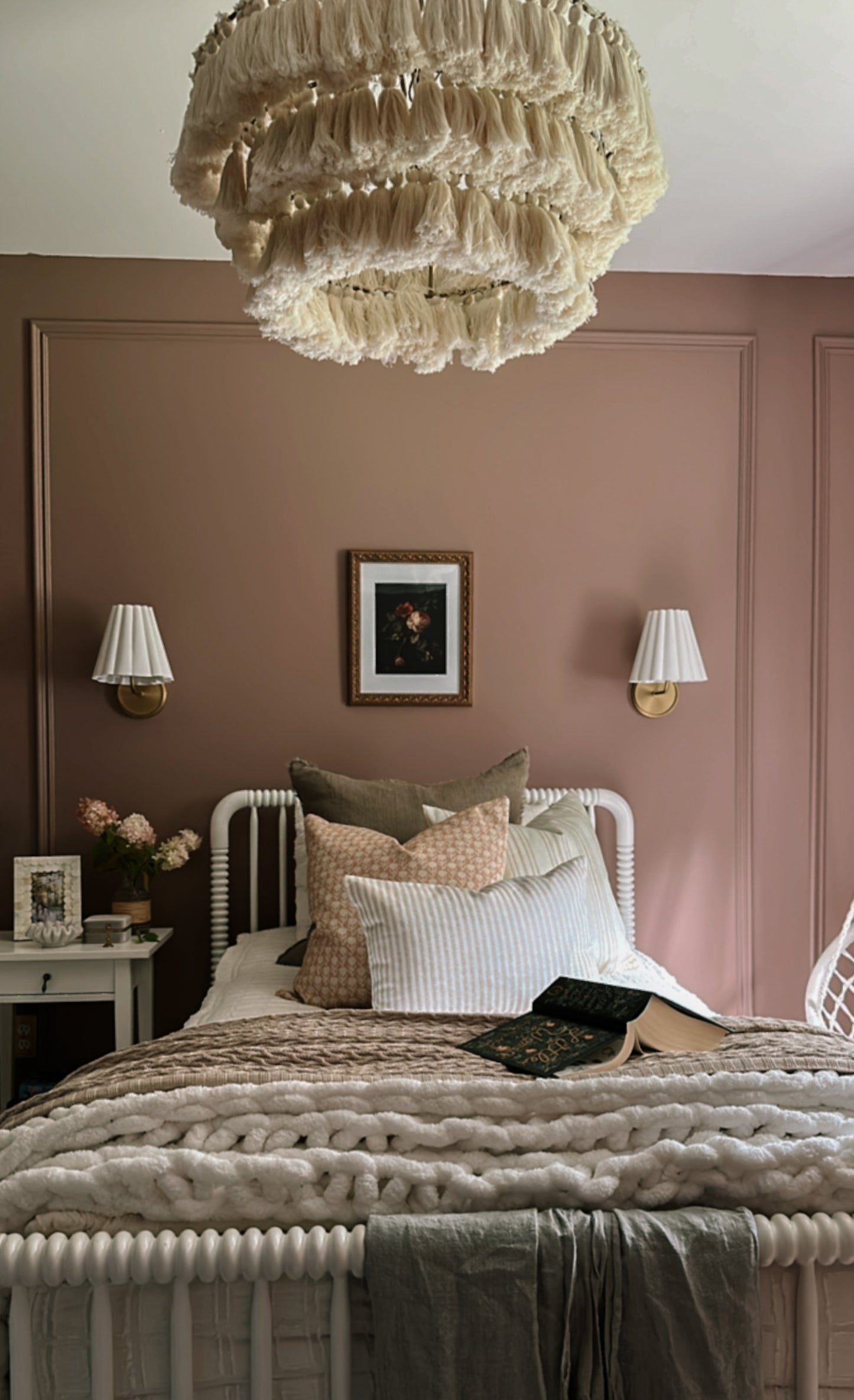 Cozy bedroom with pink walls, a bed with pillows, and decorative lighting.
